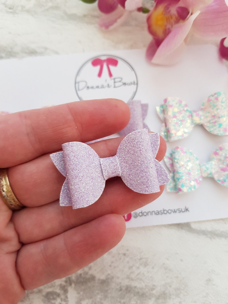Peut inclure: Un n&oelig;ud en paillettes de couleur violet clair avec un centre blanc. Le n&oelig;ud est fait &agrave; la main et est parfait pour ajouter une touche d'&eacute;clat &agrave; n'importe quelle tenue.