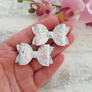 Peut inclure: Deux n&oelig;uds pour cheveux en paillettes blanches avec des paillettes iris&eacute;es et bleu pastel et rose. Les n&oelig;uds sont nou&eacute;s en un simple n&oelig;ud.