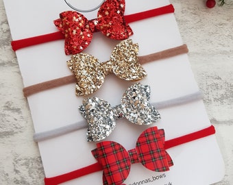Puede incluir: Cuatro diademas para bebés con lazos de purpurina en rojo, dorado y plateado, y un lazo a cuadros rojo y verde. Las diademas están en una tarjeta blanca con el texto "Donna's Bows" y redes sociales.