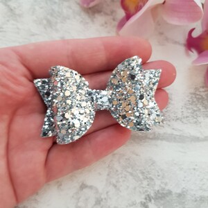Peut inclure: Un n&oelig;ud en paillettes argent&eacute;es avec une boucle centrale. Le n&oelig;ud est tenu dans une main.