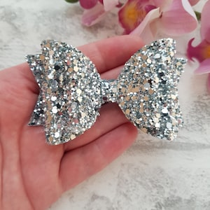 Peut inclure: Un n&oelig;ud en paillettes argent&eacute;es avec une finition scintillante. Le n&oelig;ud est fait de tissu et a une boucle &agrave; l'arri&egrave;re pour l'attacher aux cheveux.