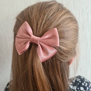 May include: A dusty rose satin hair bow tied in a simple bow shape.