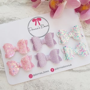 Peut inclure: Six n&oelig;uds en paillettes pour cheveux en rose, violet et blanc sur un fond blanc. Les n&oelig;uds sont dispos&eacute;s en trois rang&eacute;es de deux. Le texte "Donna's Bows" est dans un cercle en haut de la carte. Les poign&eacute;es de m&eacute;dias sociaux "@donnas_bows" et "@donnasbows.uk" sont en bas de la carte.