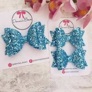 May include: Two turquoise glitter hair bows on white cards with the text "Donna's Bows" and social media handles.