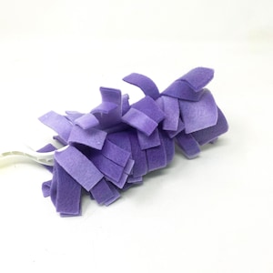 May include: A purple microfiber duster with a white plastic handle. The duster is made of many small, soft fibres that are designed to pick up dust and dirt.