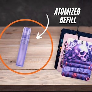 May include: A purple atomizer refill bottle is highlighted with an orange circle. Three air freshener tags are displayed, one with a skull and floral design, and the text "Book Club". The text "ATOMIZER REFILL" is also visible.