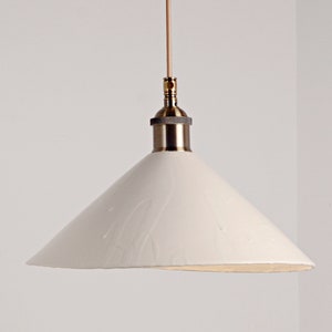 May include: A white ceramic pendant light with a brass fixture. The shade is a cone shape with a slightly uneven edge.