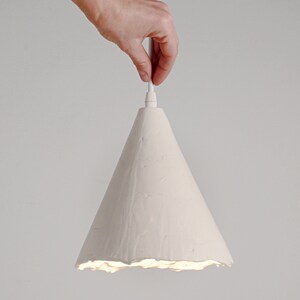 Stylish artisan ceramic pendant lamp for kitchen island lighting with soft shadow ambiance. A white cone-shaped pendant light fixture with a textured surface. The light is hanging from a white cord.