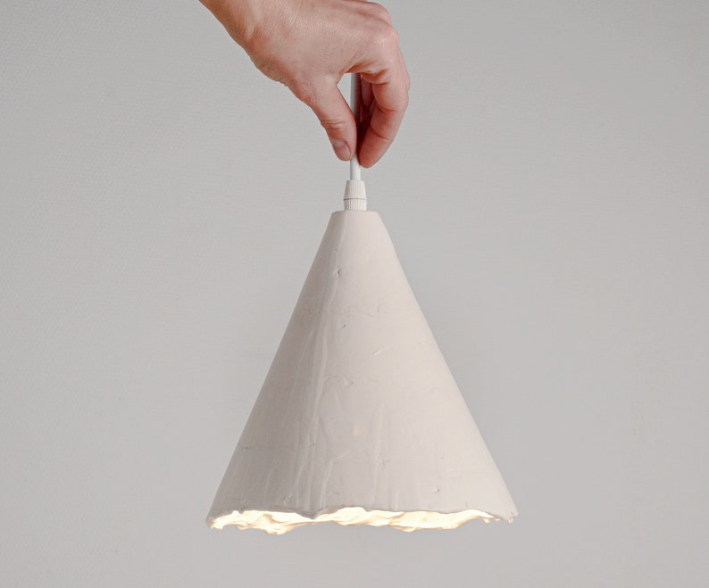 Stylish artisan ceramic pendant lamp for kitchen island lighting with soft shadow ambiance. A white cone-shaped pendant light fixture with a textured surface. The light is hanging from a white cord.