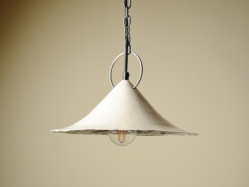 Rustic ceramic pendant lamp for kitchen island with textured organic edge and chain suspension. A white, cone-shaped pendant light fixture with a black chain and ring.
