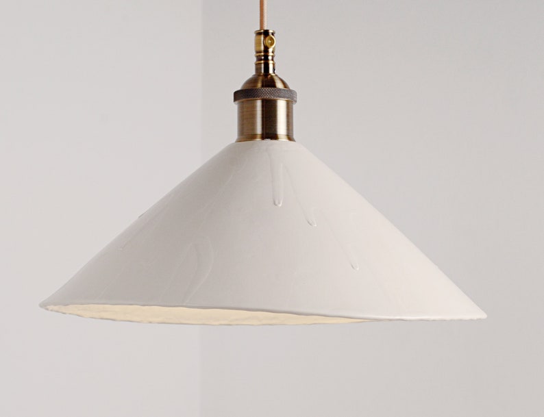 May include: A white ceramic pendant light with a brass fixture and a cone-shaped shade. The shade has a textured surface that resembles dripping water.