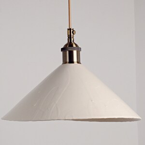 May include: A white ceramic pendant light with a cone-shaped shade and a brass fixture.