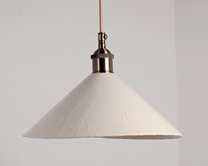 May include: A white ceramic pendant light with a cone-shaped shade and a brass fixture.
