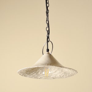 White farmhouse pendant light for kitchen island lighting. A white ceramic pendant light with a textured, rippled surface. The light is suspended from a black chain and has a simple black ring at the top.