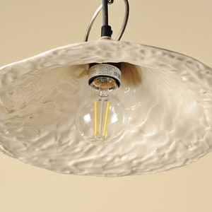 Elegant kitchen island pendant featuring handmade white ceramic shade. White ceramic pendant light fixture with a textured surface and a clear light bulb.