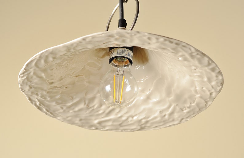 Elegant kitchen island pendant featuring handmade white ceramic shade. White ceramic pendant light fixture with a textured surface and a clear light bulb.
