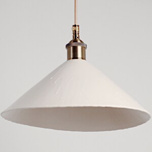 May include: A white ceramic pendant light with a brass fitting. The shade is cone-shaped and has a textured surface.