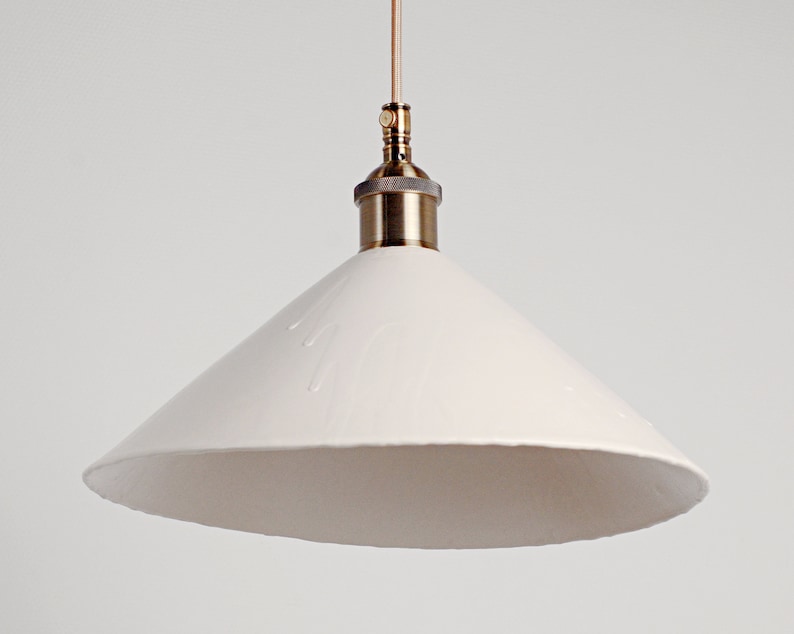 May include: A white ceramic pendant light with a brass fitting. The shade is cone-shaped and has a textured surface.