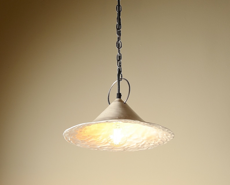 Artisan ceramic hanging kitchen lamp with sculptural handmade shade. A white ceramic pendant light fixture with a textured, wavy surface. The light is suspended from a chain and has a simple, modern design.