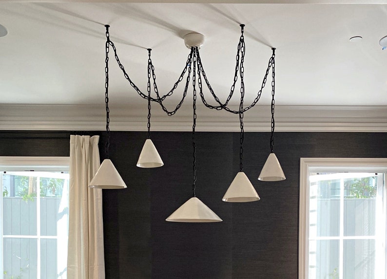 Customisation options. Contemporary handmade ceiling pendant light in ceramic material designed for kitchen island decor. A modern chandelier with six white cone-shaped shades hanging from black chains.