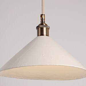 May include: A white ceramic pendant light with a brass fixture and a cone-shaped shade.