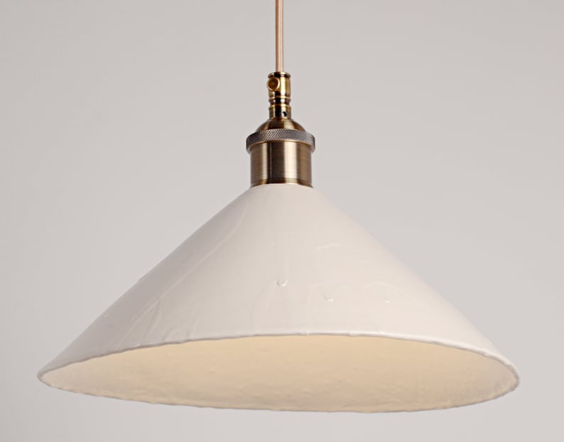 May include: A white ceramic pendant light with a brass fixture and a cone-shaped shade.