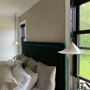 Wabi sabi ceramic pendant light with organic handmade form. Two white pendant lights hanging from the ceiling. The room has a window with black trim and a view of green trees.