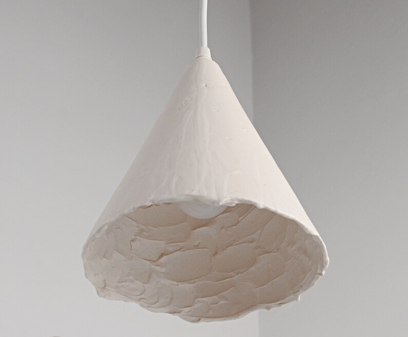 Modern kitchen island lighting featuring sculptural ceramic pendant light with soft ambient glow. A white cone-shaped pendant light fixture with a textured surface.