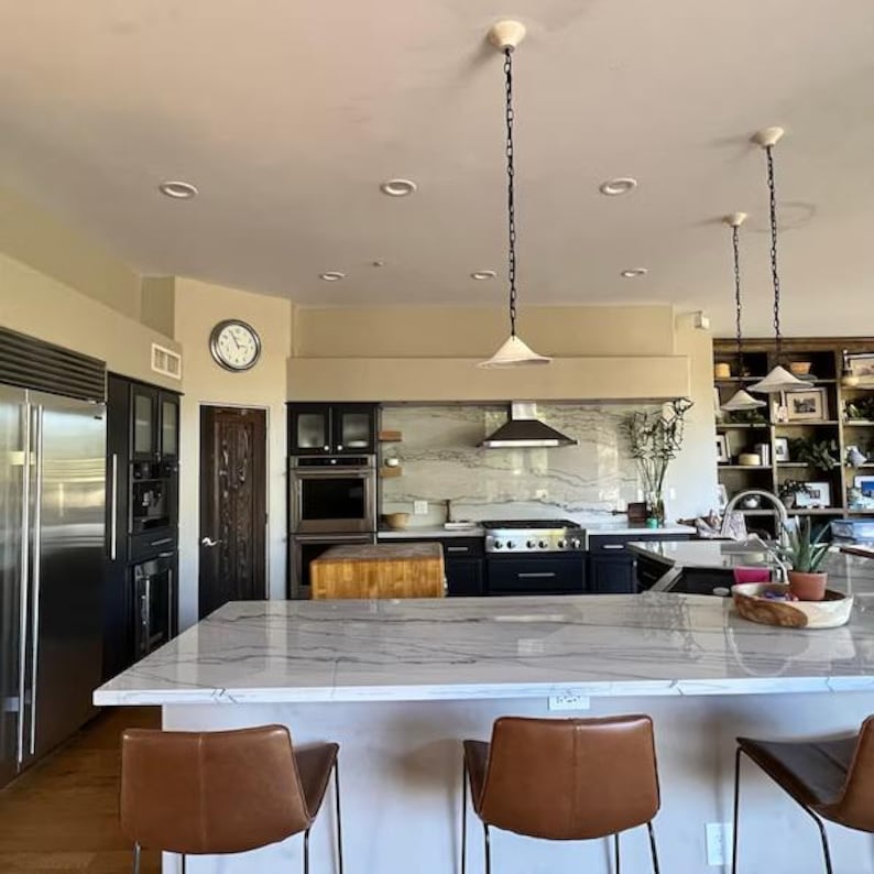 3 ceramic pendants lamps whith a chains hanging in modern skandi kitchen under kitchen island and dinner table.