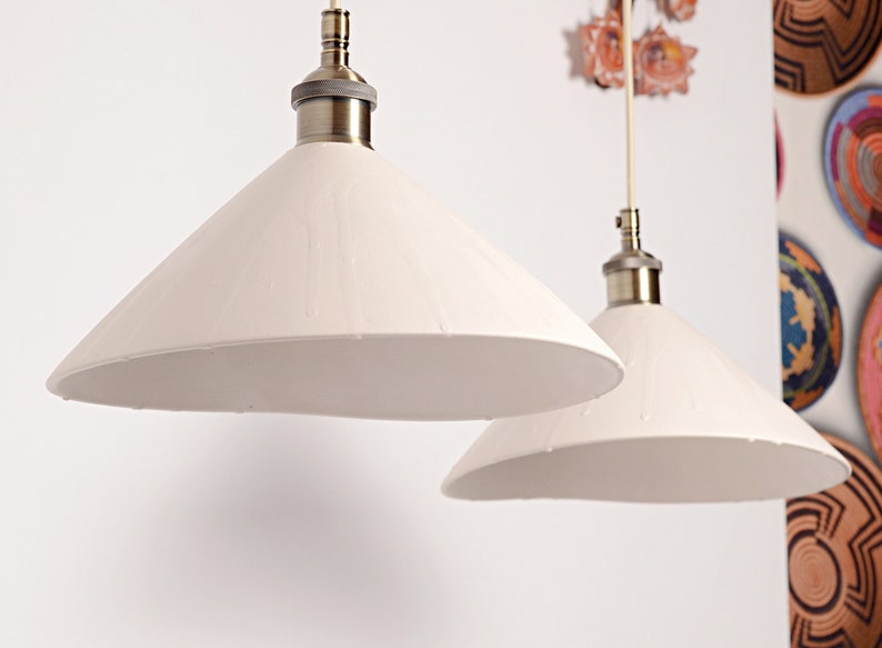 May include: Two white cone-shaped lampshades with brass fixtures hanging from the ceiling.