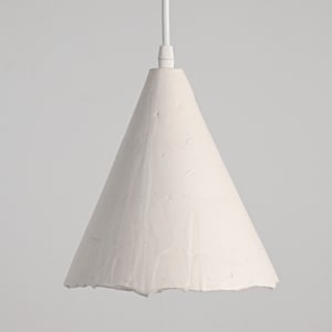 Minimalist kitchen pendant lighting with textured ceramic shade in modern farmhouse interior. A white cone-shaped pendant light fixture with a textured surface.