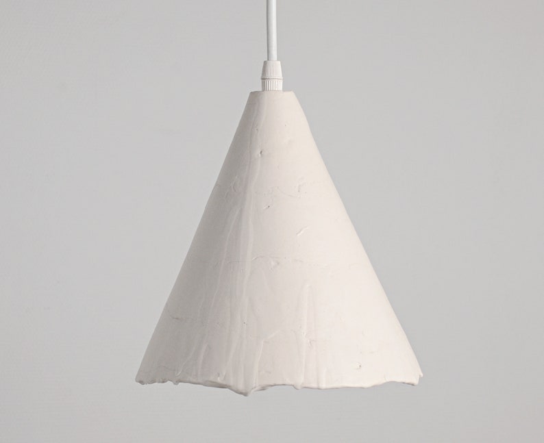 Minimalist kitchen pendant lighting with textured ceramic shade in modern farmhouse interior. A white cone-shaped pendant light fixture with a textured surface.