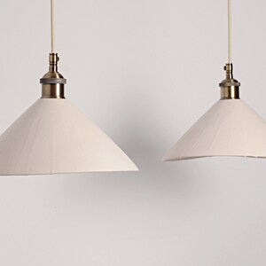 May include: Two white cone-shaped pendant lights with brass fixtures hanging from the ceiling against a white background.
