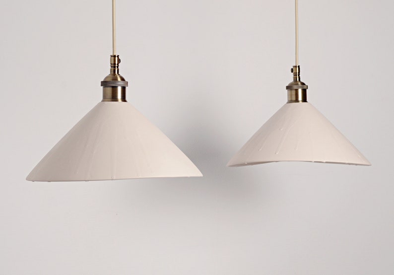 May include: Two white cone-shaped pendant lights with brass fixtures hanging from the ceiling against a white background.