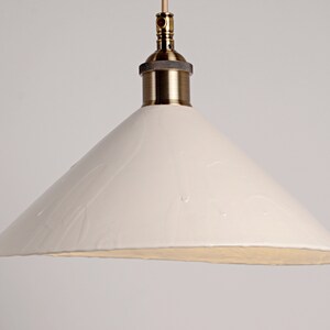 May include: A white ceramic pendant light with a brass fitting. The shade is cone-shaped and has a textured surface.
