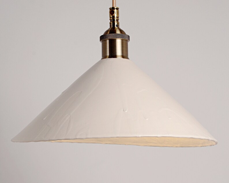 May include: A white ceramic pendant light with a brass fitting. The shade is cone-shaped and has a textured surface.