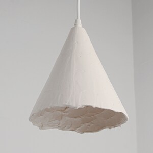 Kitchen island lighting setup with handmade ceramic ceiling pendant in neutral interior decor. A white, cone-shaped pendant light fixture with a textured surface.