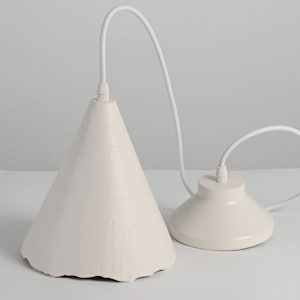 Elegant modern ceramic pendant lamp suspended over kitchen island in bright contemporary home. A white pendant light with a cone-shaped shade and a round, flat base. The light is suspended from a white cord.
