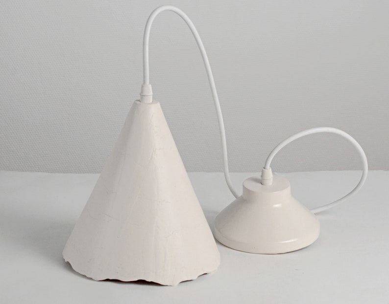Elegant modern ceramic pendant lamp suspended over kitchen island in bright contemporary home. A white pendant light with a cone-shaped shade and a round, flat base. The light is suspended from a white cord.