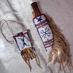 May include: A small rectangular pouch with a long strap and a knife sheath, both featuring white, blue, and red geometric beadwork. The pouch has a fringe of tan leather strips and metallic beads, while the sheath has long tan leather fringe.