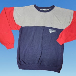 May include: A long-sleeved sweatshirt with a red, gray, and blue color block design. The sweatshirt has a white logo that says "Athletic Supply" on the front.