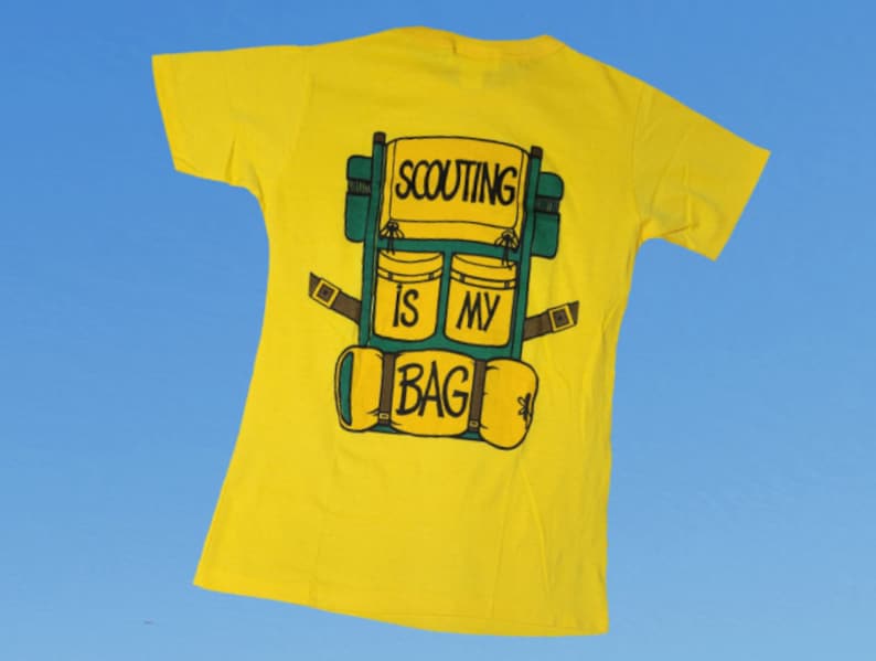 May include: Yellow t-shirt with a green and brown cartoon backpack on the back. The backpack has the text "SCOUTING IS MY BAG" on it.