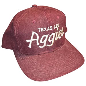 May include: A maroon baseball cap with a white embroidered logo that says "Texas A&M Aggies".