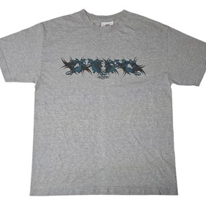 May include: A gray short-sleeved t-shirt with a blue and black graphic design of stylized flames. The graphic design includes the text "Element" in a black font.