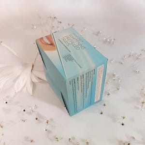 Può includere: Una scatola blu con la scritta "Whitening Prefilled Trays" su di essa. La scatola è appoggiata su una superficie bianca con piccoli fiori bianchi.