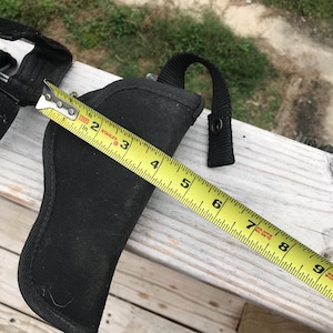 May include: A black nylon holster with a loop handle and snap closure, measured with a yellow Stanley tape measure. The holster is approximately 13 cm long.