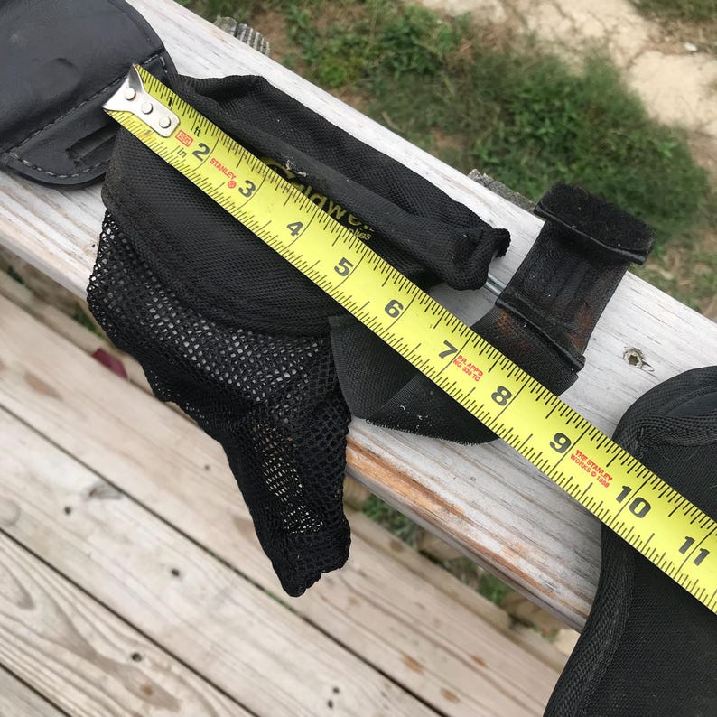 May include: Black equestrian equipment, including a mesh-lined boot protector, a leather-like strap, and a black pad. A yellow measuring tape shows the boot protector is approximately 18 cm long.