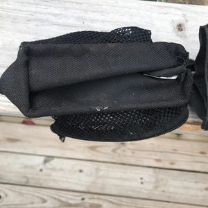 May include: Black mesh bag with a zippered closure and a drawstring top. The bag is made of a durable, breathable material, and is designed to hold items. The bag is folded and appears to be empty.