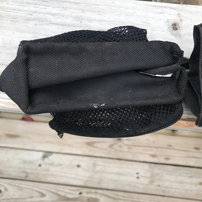 May include: Black mesh bag with a zippered closure and a drawstring top. The bag is made of a durable, breathable material, and is designed to hold items. The bag is folded and appears to be empty.