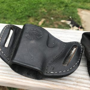 May include: Black leather holster with white stitching. The holster features two belt slots and a stamped logo reading "Bulldog Cases". Designed to securely hold a firearm.